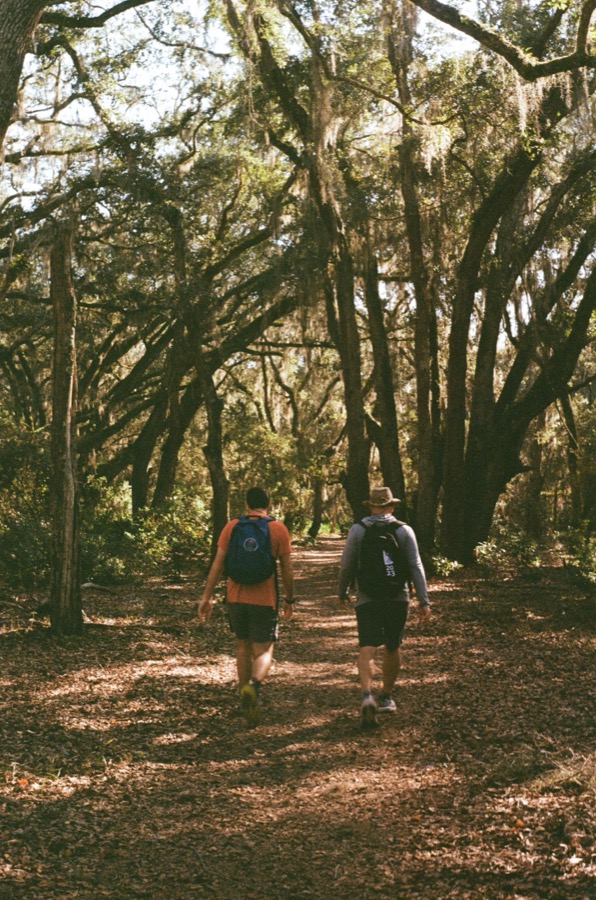 Two friends hiking the Parallel Trail beneath moss-draped oaks